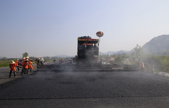2019年8月，宜春經(jīng)開區(qū)S311路面攤鋪現(xiàn)場(chǎng)，工友們輔助路面兩側(cè)的分料、補(bǔ)窩等作業(yè)